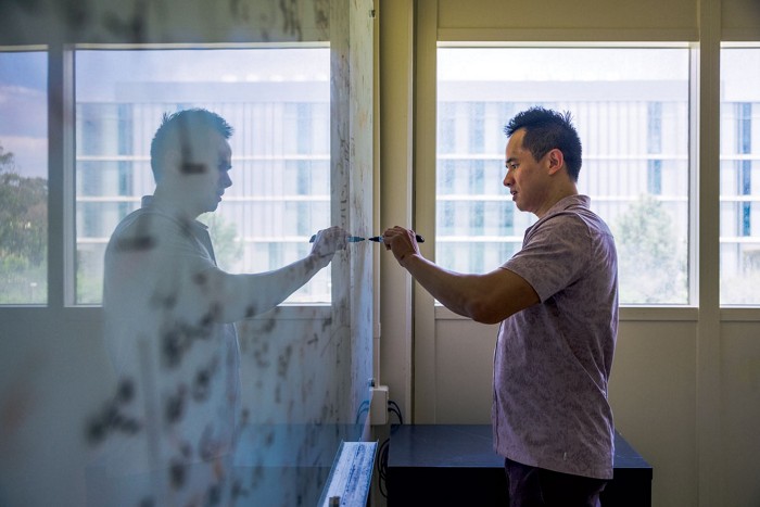 Joel Yuen-Zhou stands parallel to a whiteboard and writes.