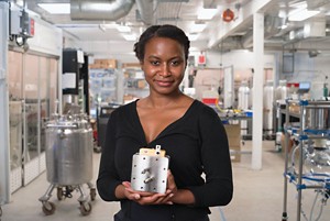A person holding a reactor prototype stands a safe distance from a chemical plant.