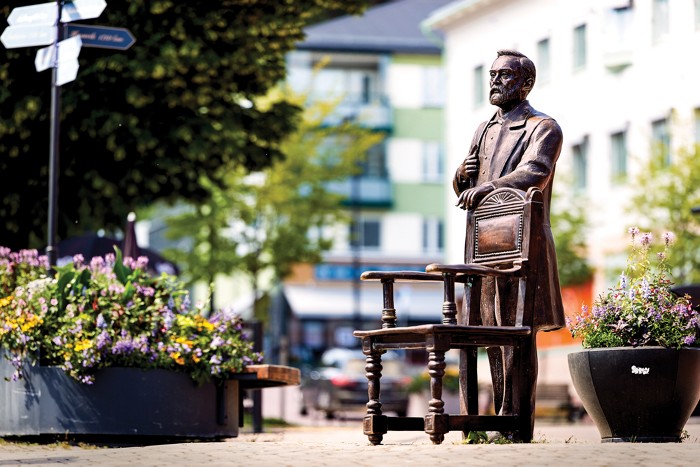 A photo of a metal statue of Alfred Nobel standing behind a chair.