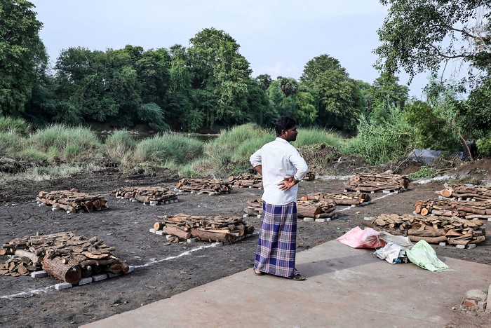 A man stands next to piles of wood arranged for the cremation of people.