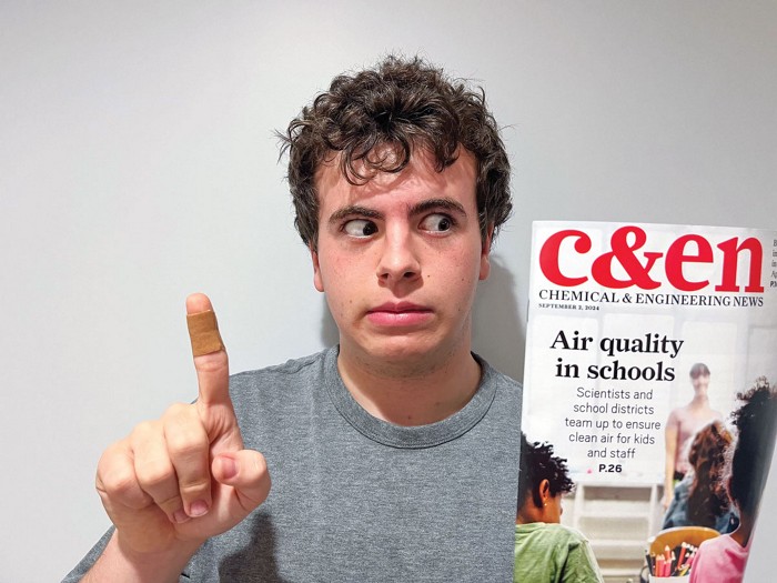 A teen with a bandage on his finger holding a copy of C&EN.