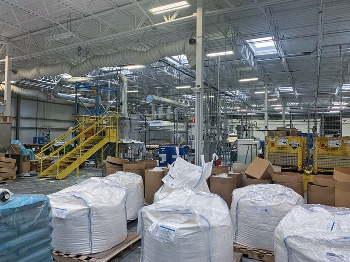 A small chemical factory and warehouse, with manufacturing equipment in the background and pallets of material in the foreground.