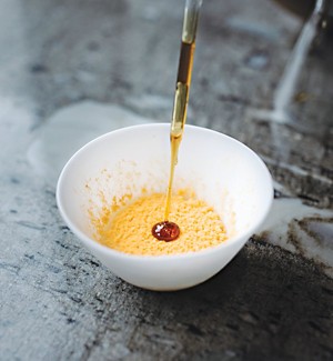 A white bowl is half filled with a fluffy orange material. The tip of a pipette is squirting a substance resembling maple syrup onto the orange fluff.