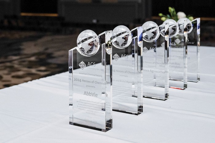Five glass awards lined up on a table.