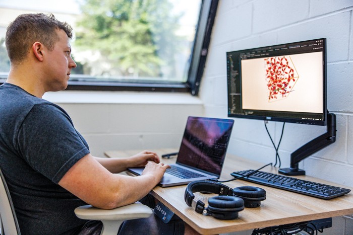 A person types on a laptop while a material is displayed on a screen