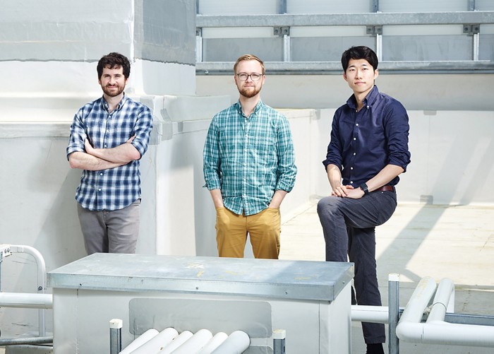 Three men pose among HVAC equipment.