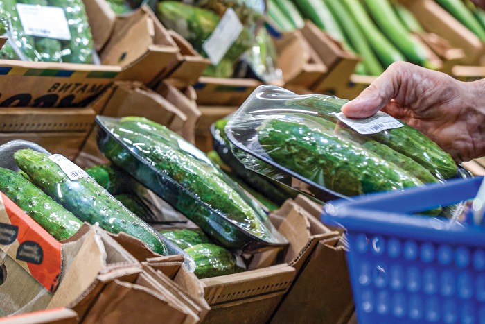 A man picks up a shrink-wrapped package of cucumbers in a grocery store.