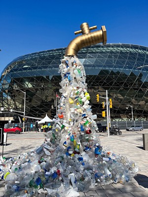 A sculpture of a giant water tap suspended on a stream of plastic waste flowing toward the ground.
