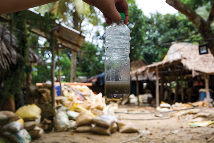 A hand holds a plastic water bottle containing a mercury solution.