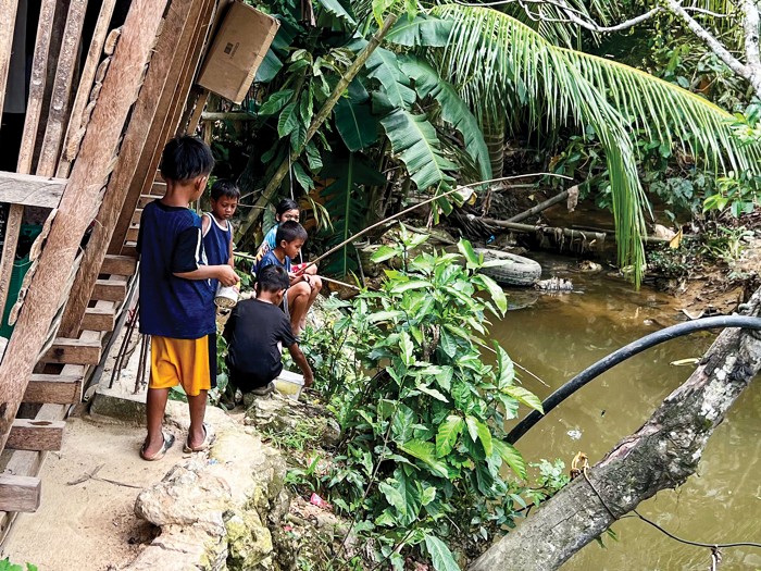 Children fishing beside a river.