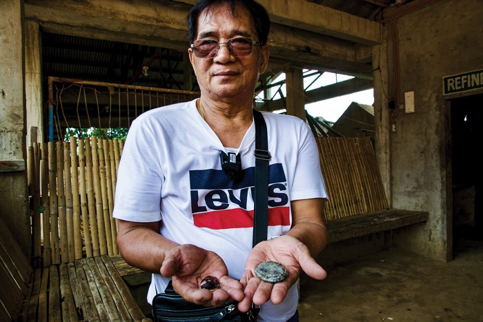 A man holds out his hands containing small metal-like objects.