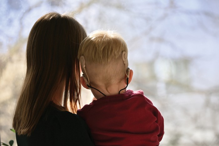 A woman holds a small boy with cochlear implants visible on the back of his head.
