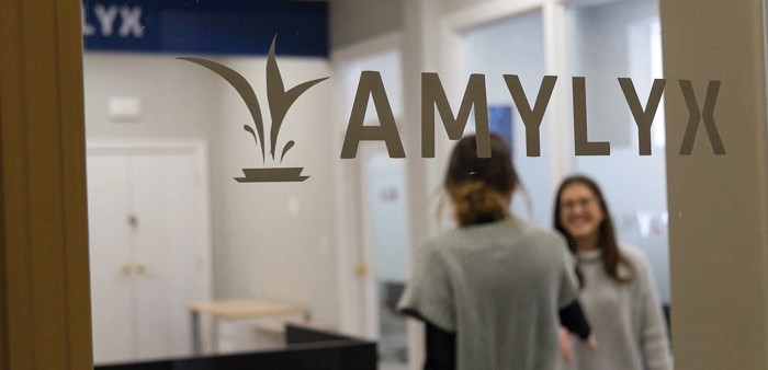 The Amylyx Pharmaceuticals logo is printed on a glass wall in an office.