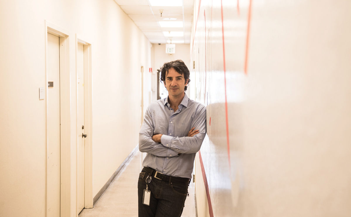 Marco Quarta leans against a wall in a hallway, his arms crossed.