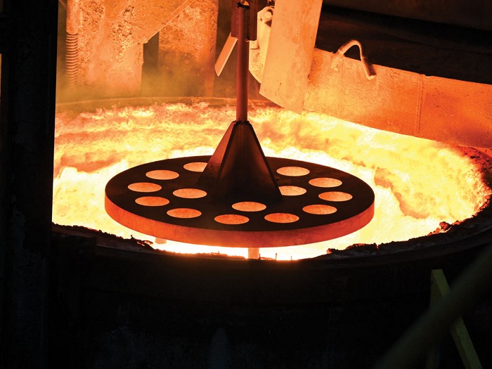 A large perforated disk held over a red, hot mixture in a drum.