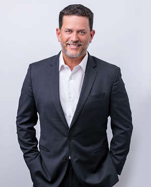 CEO Kent Rogers strikes a formal pose, wearing a dark suit and smiling.