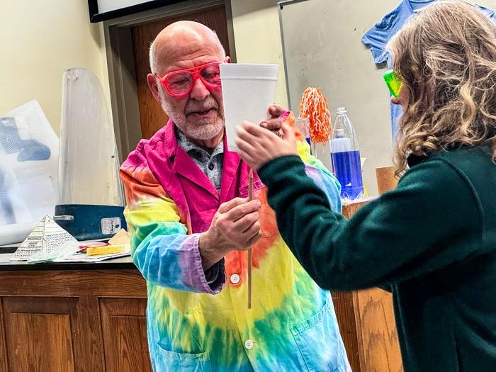 Two people wearing safety goggles in a laboratory hold a stick with a cup attached.