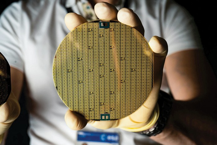 Person holding a semiconductor wafer in their gloved hand.