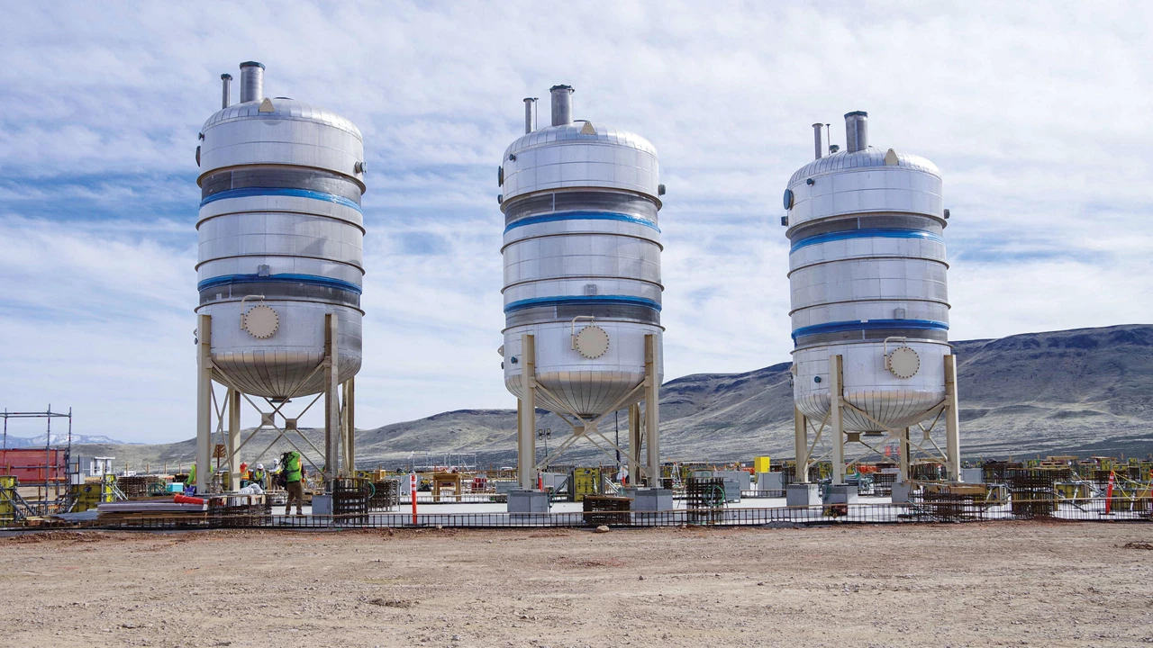 Three large cylinders on legs stand in a desert environment.