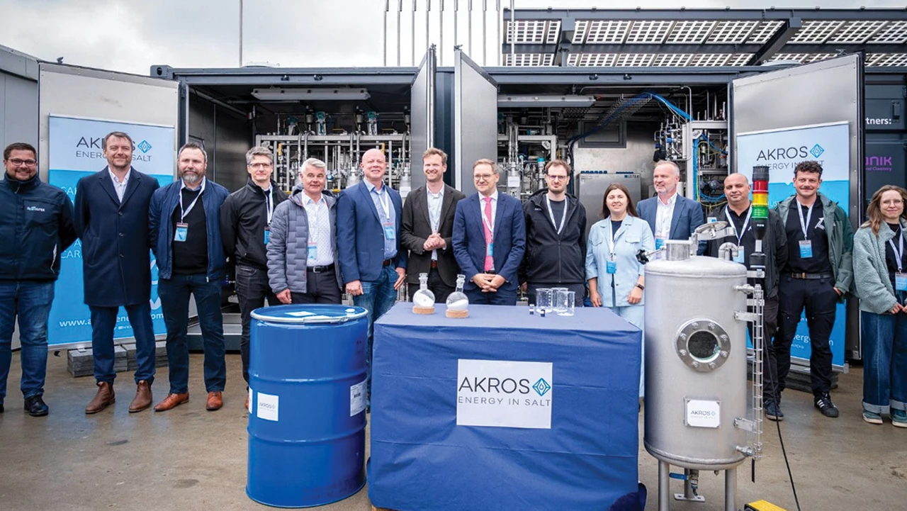 People in business attire pose in front of a facility in which snaking pipes can be seen.