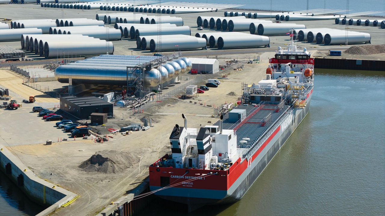 A bright-red tanker ship docked at a port covered with a number of large cylindrical tanks.