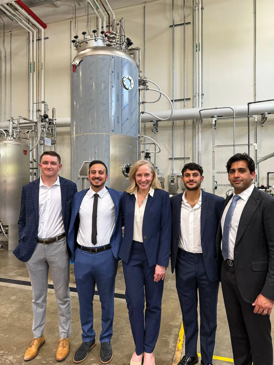 A group of five people, including Virginia governor Abigail Spanberger, pose in front of chemical equipment.