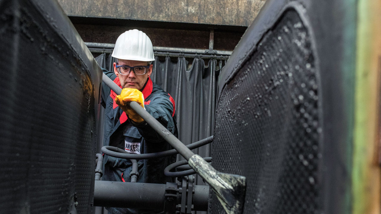 A worker in a hard hat and other protective gear uses a tool to clean a vent.