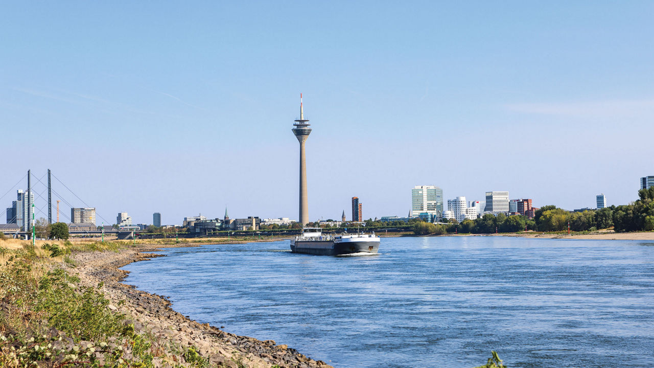 A parched riverbank and a barge with a city skyline in the background.