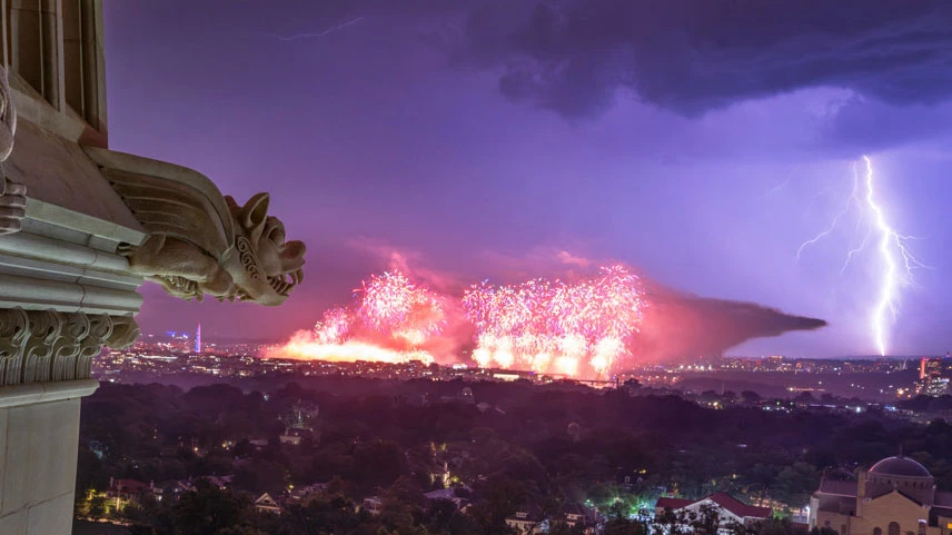A photo of lightning strikes and fireworks over Washington, DC, as seen from up high in a tower at the Washington National Cathedral.