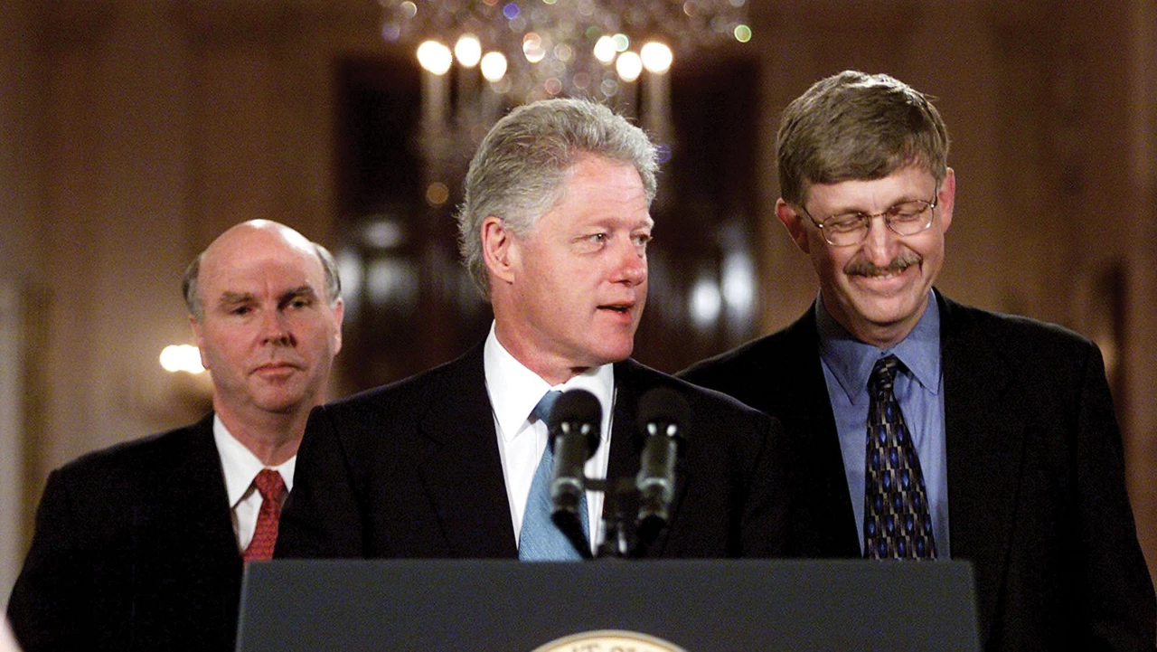 Three men stand behind a podium with Bill Clinton speaking behind the microphone in the middle, with glowing chandeliers overhead in the background.