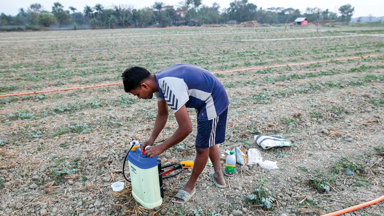 A man in shorts and a T-shirt mixes chemicals in a plastic container.