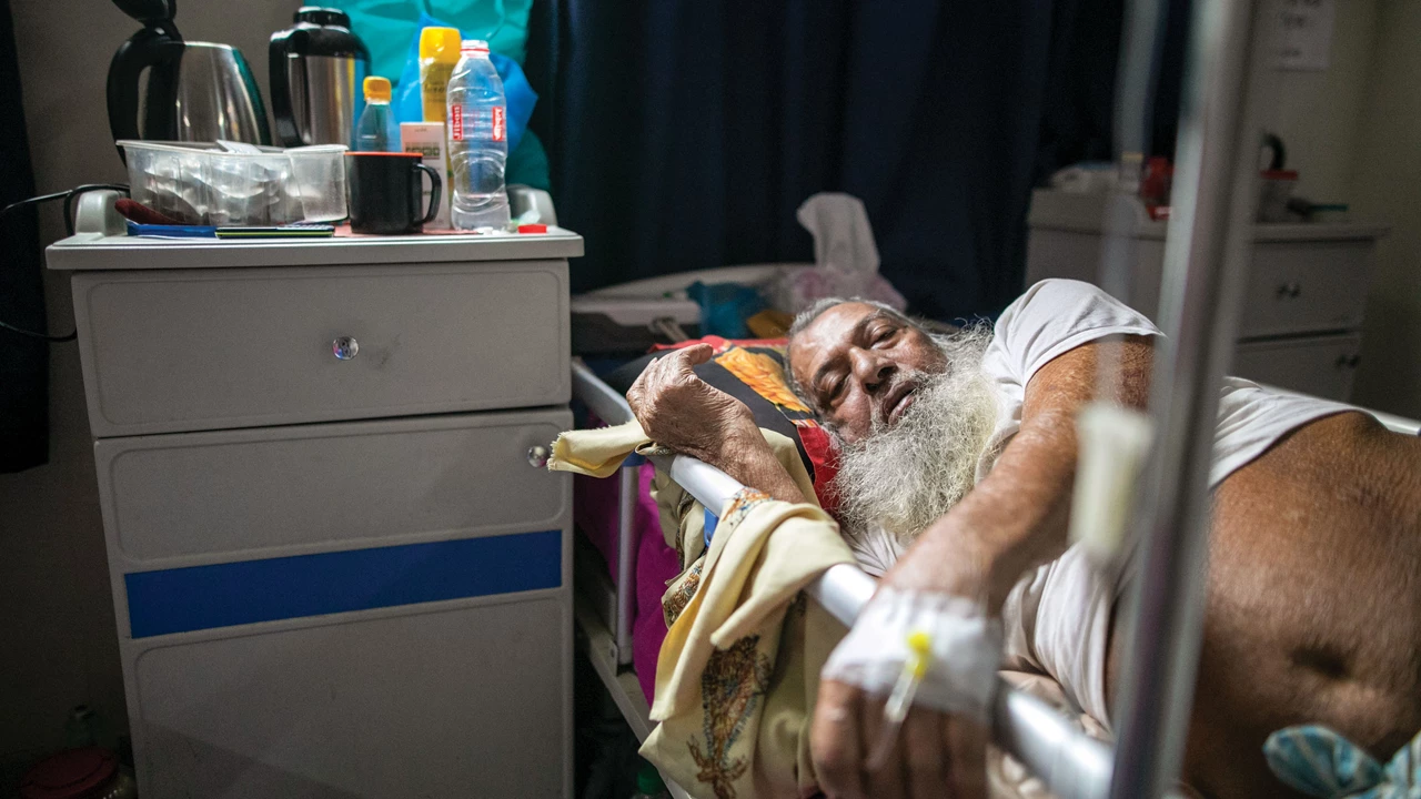 A man lies on a hospital bed with an IV drip connected to his veins.