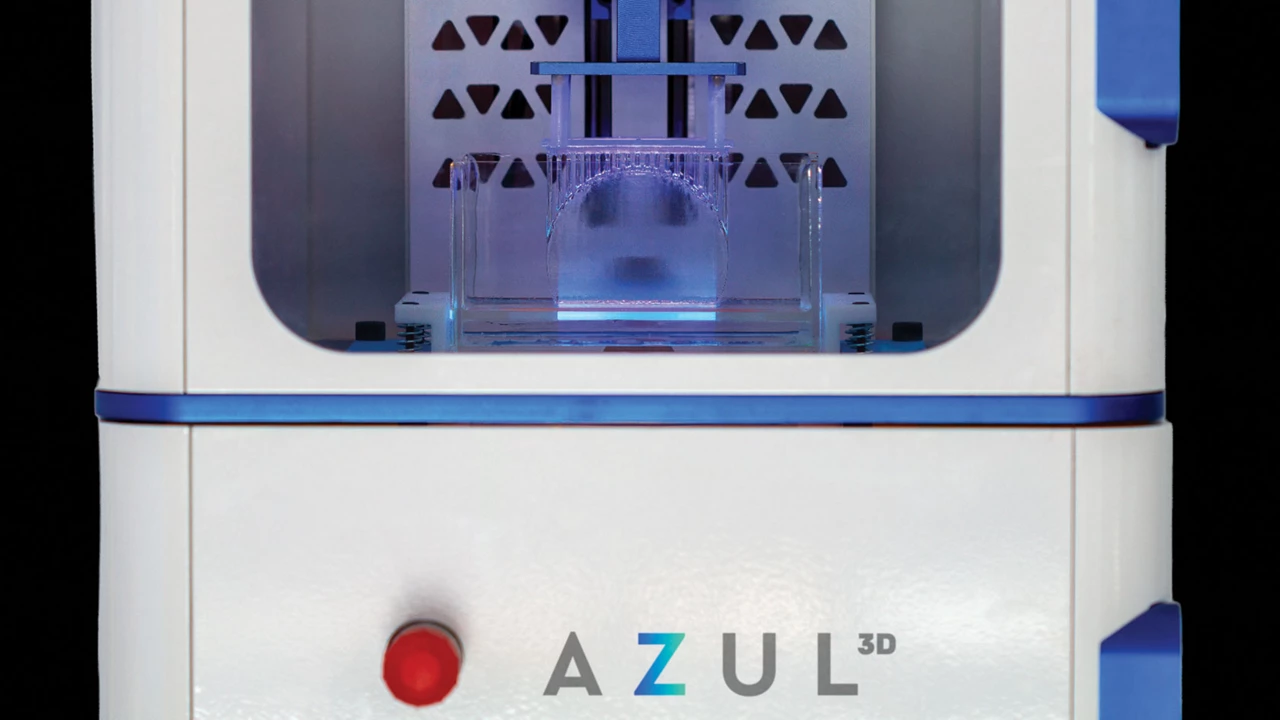 A close-up of a 3D printer shows a blue glow lighting a transparent structure from below.