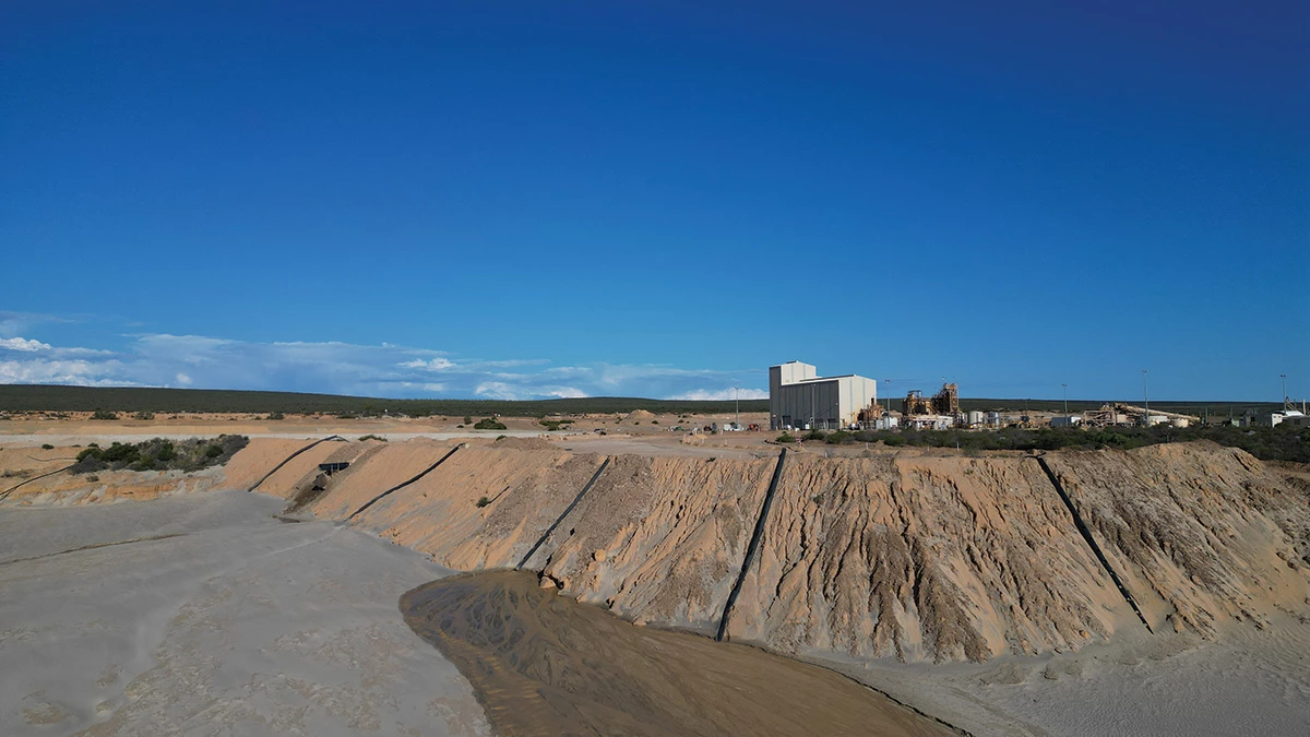 A panoramic photograph of a mining facility with gray-brown earth and a white building in the distance.
