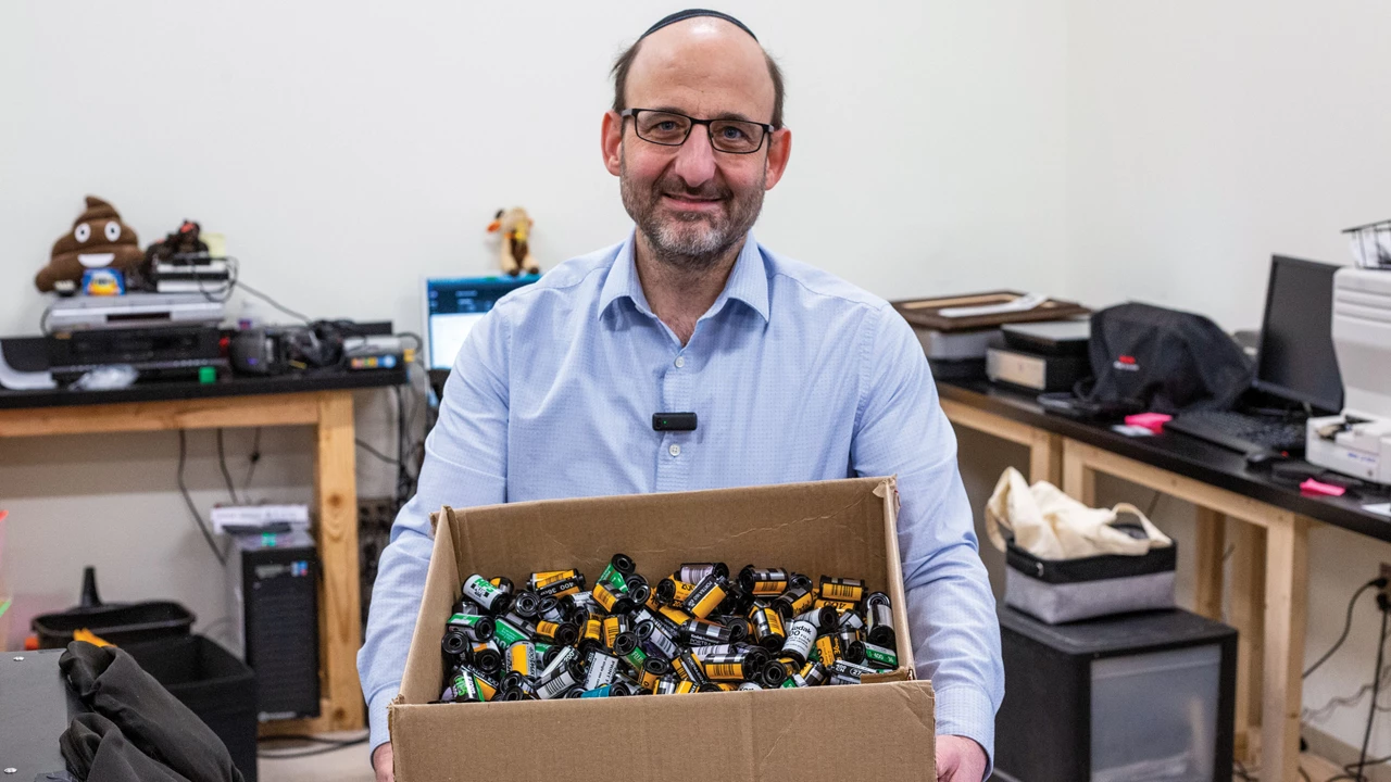 A man holds a large box of empty film cassettes.