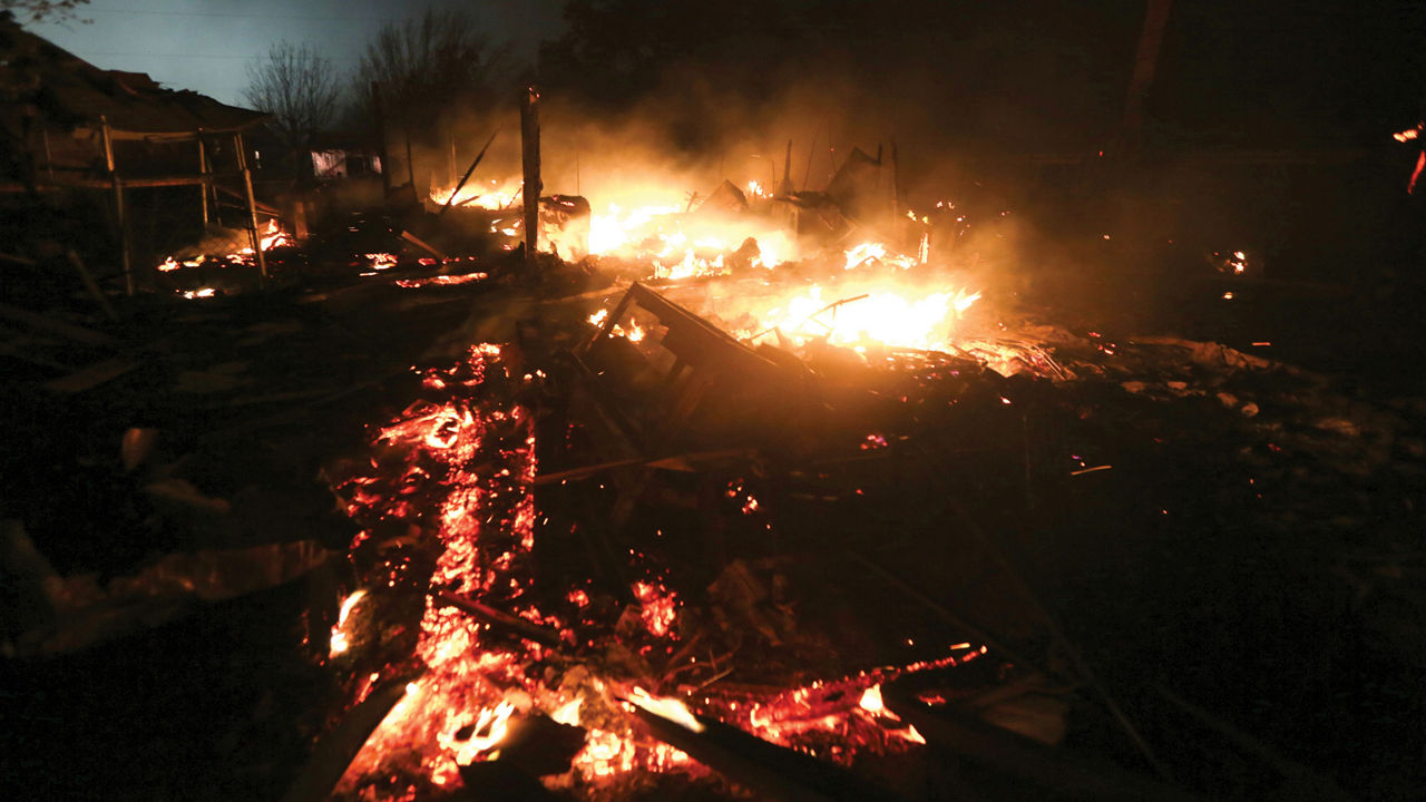 A hillside home destroyed by an explosion at a fertilizer plant burns as the sun comes up.