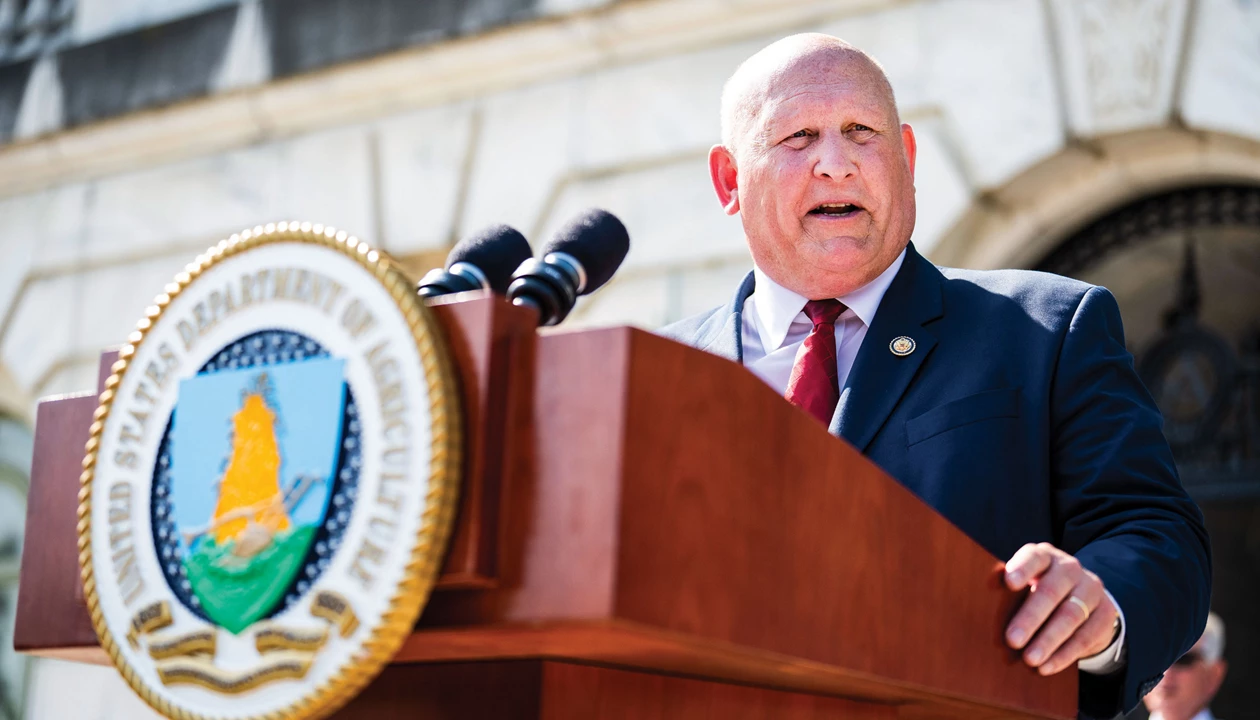 A man in a suit stands at a lectern with a microphone and the seal of the US Department of Agriculture in front.