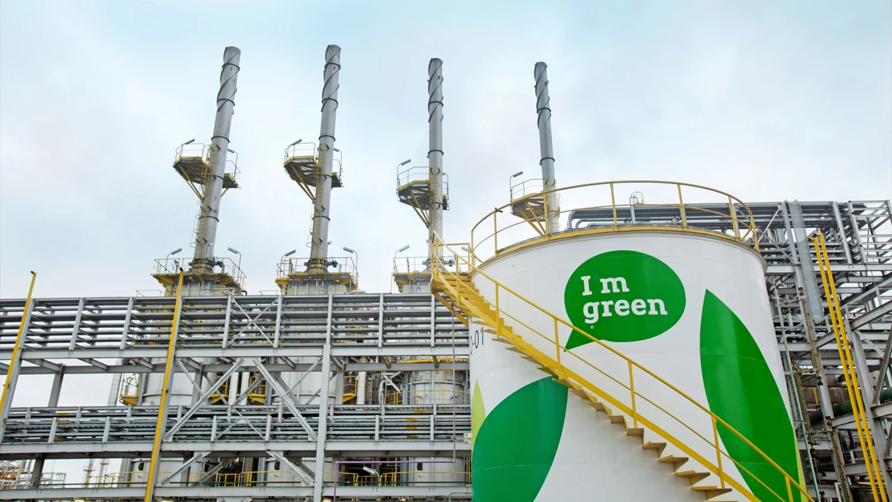 A storage tank labeled “I m green” sits in front of a petrochemical facility.