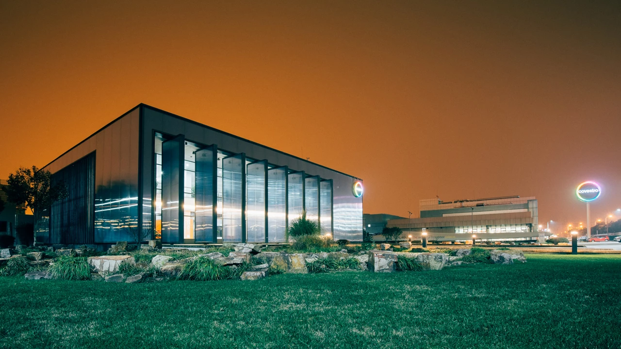 An office building at night. The building has a round Covestro sign hanging on it, and the night glimmers orange.