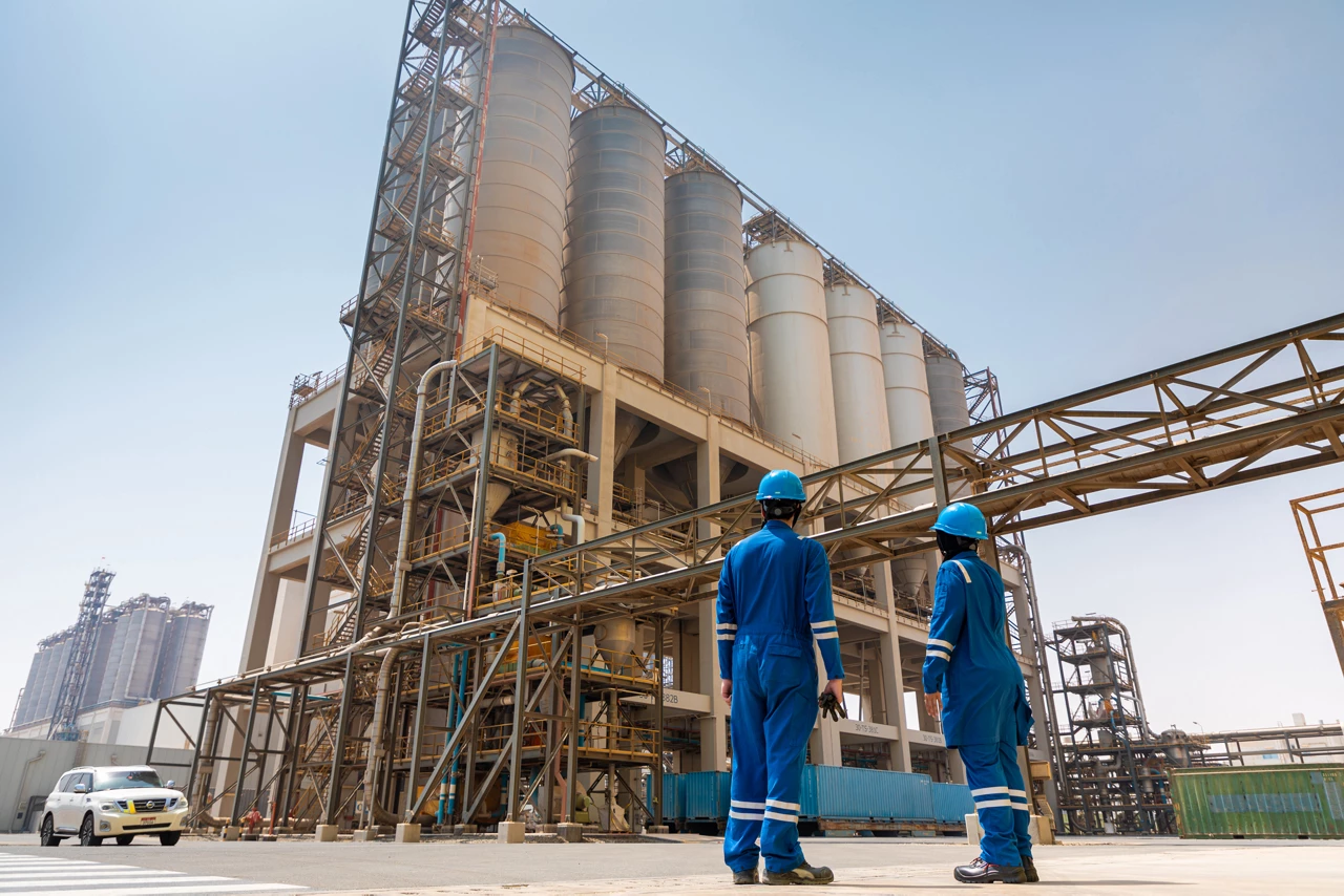 Two workers in blue work suits look at a petrochemical plant.