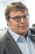 Retrato da licença de Peter. Ele está usando óculos, uma camisa de botão e uma jaqueta.