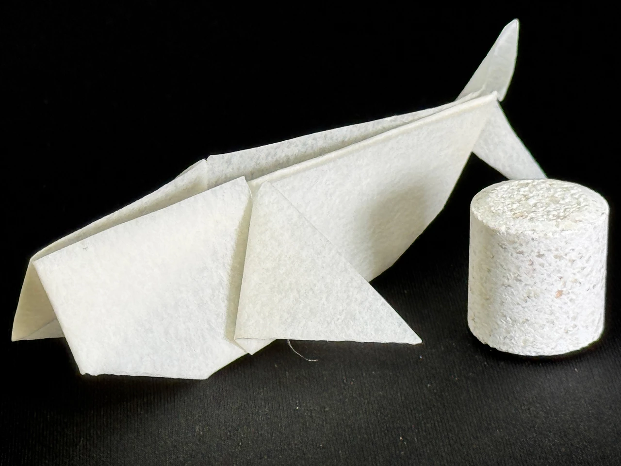 An origami whale made of a matte translucent white material and a mottled white cylinder.