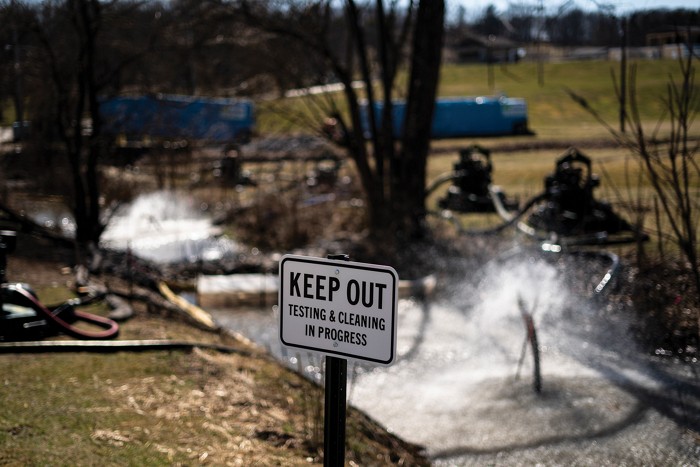 In front of a creek is a sign saying Keep Out, testing and cleaning in progress.
