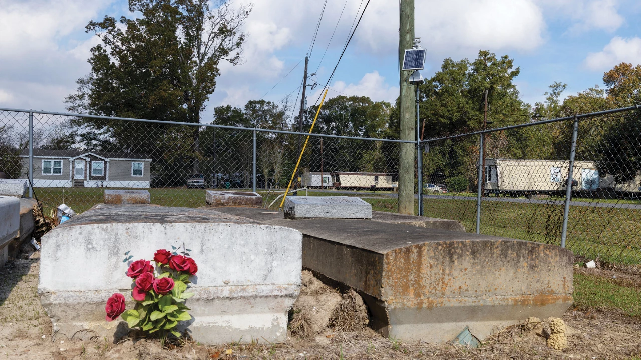 Air monitor with a solar panel stands behind two headstones in a cemetery.