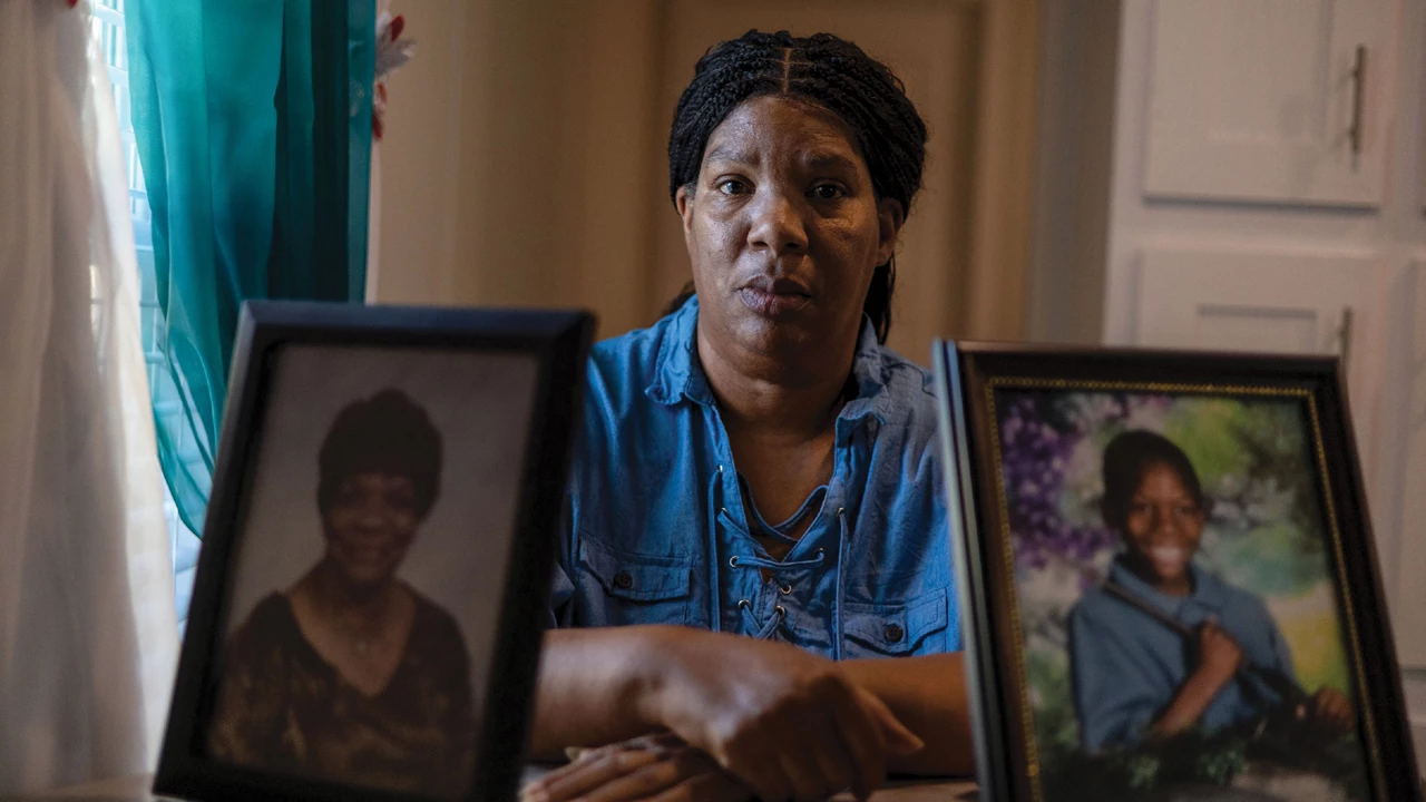 A woman in a blue shirt sits at a table behind two large framed photos.