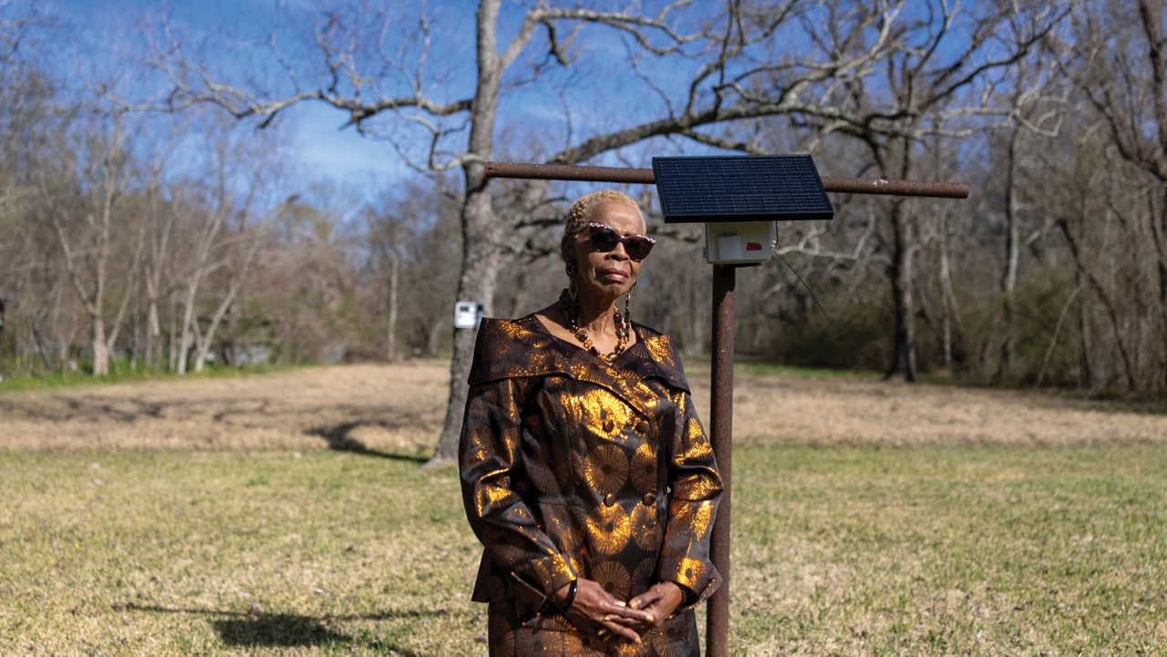 Woman wearing sunglasses and a printed top stands in front of an air monitor that’s fixed to a T-pole.