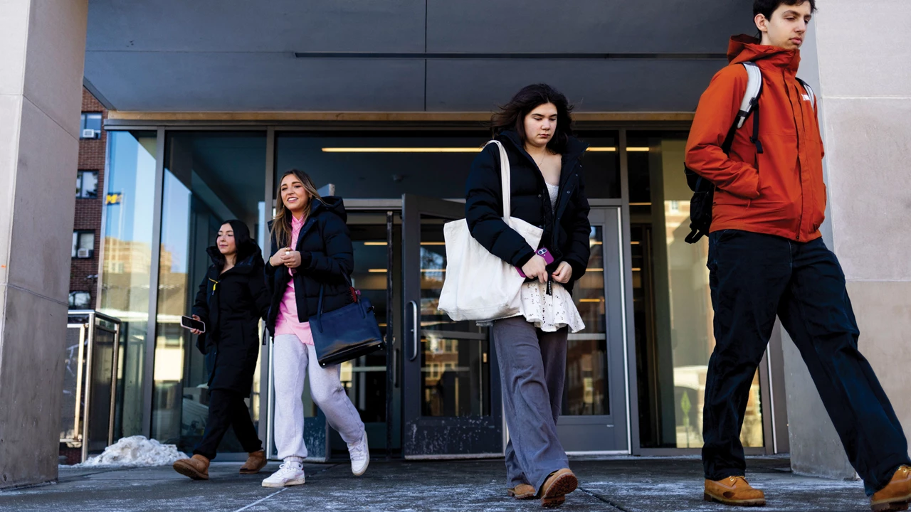 Four people wearing casual pants and jackets walk out of a building.