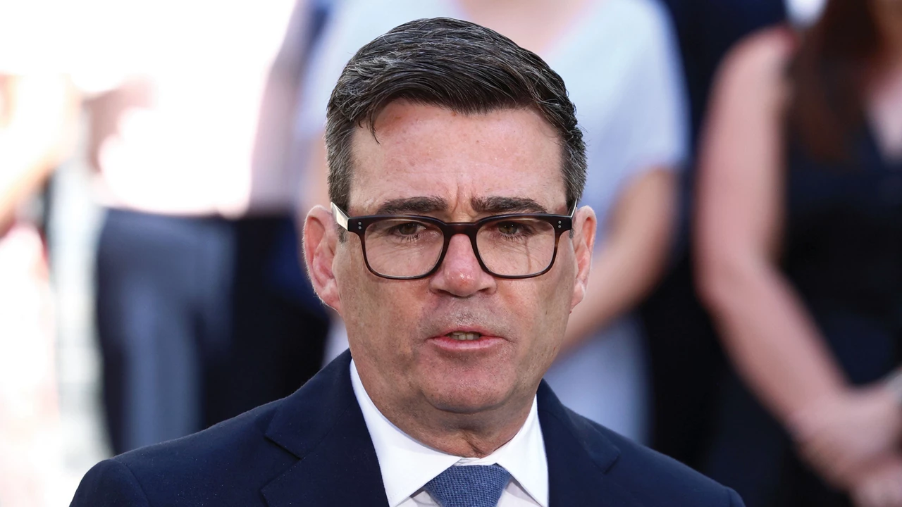 A man wearing glasses along with a suit jacket, white shirt, and tie appears to be speaking.