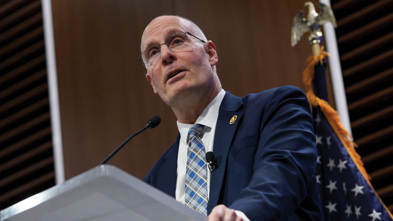Representative John Moolenaar, wearing a suit and tie, stands at a lectern with a US flag behind him.