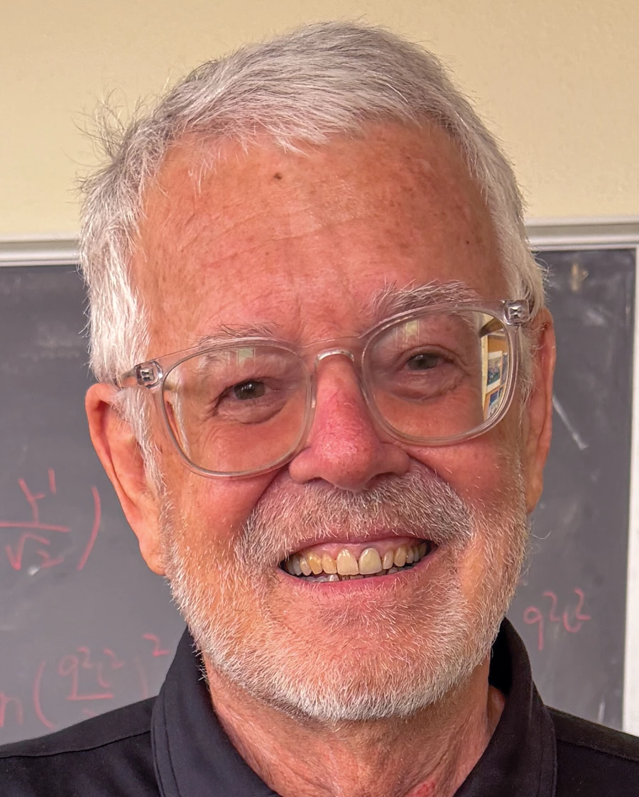 A man in a dark-gray collared shirt and glasses smiles at the camera.